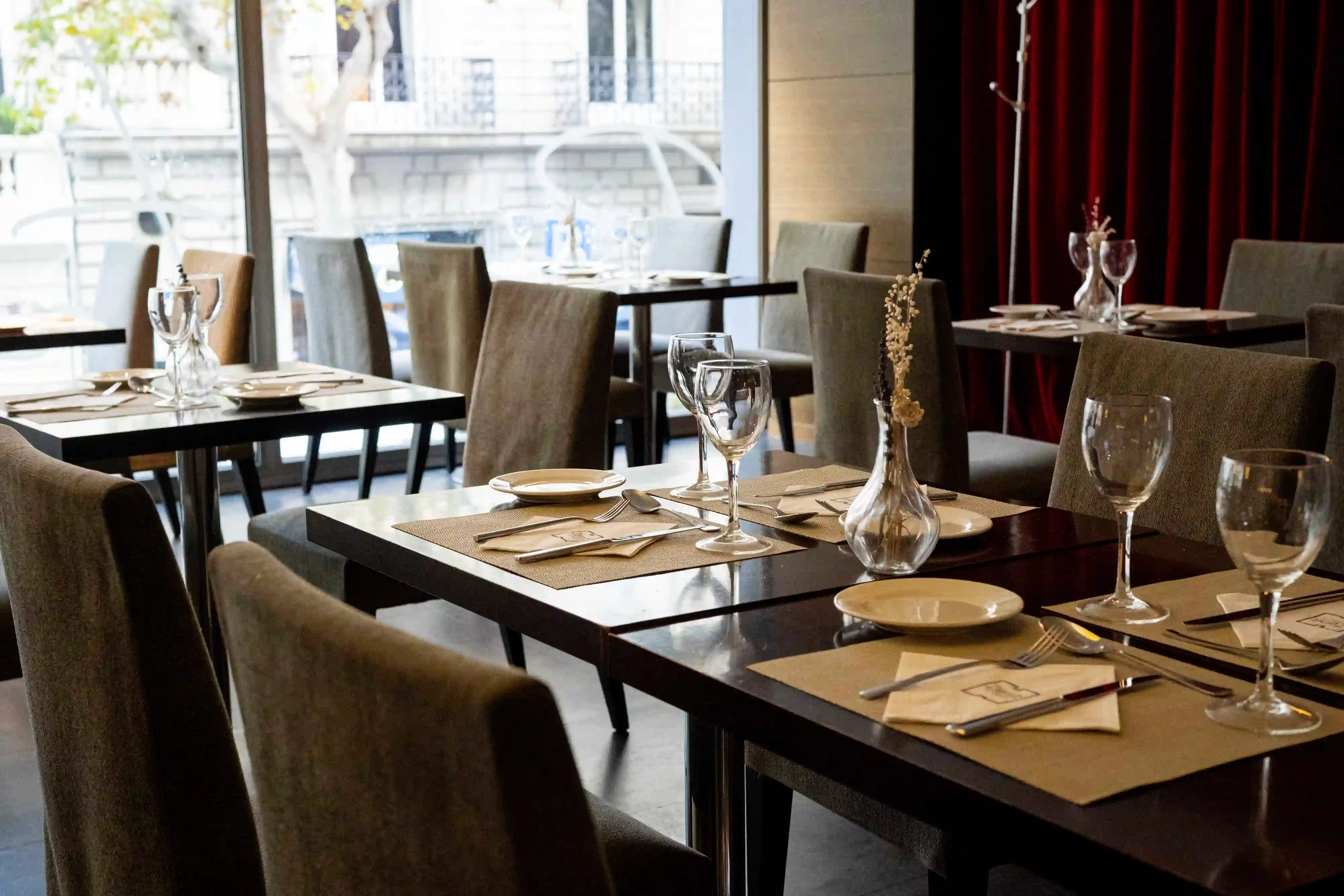 Comedor con mesas puestas, manteles y copas junto a un gran ventanal